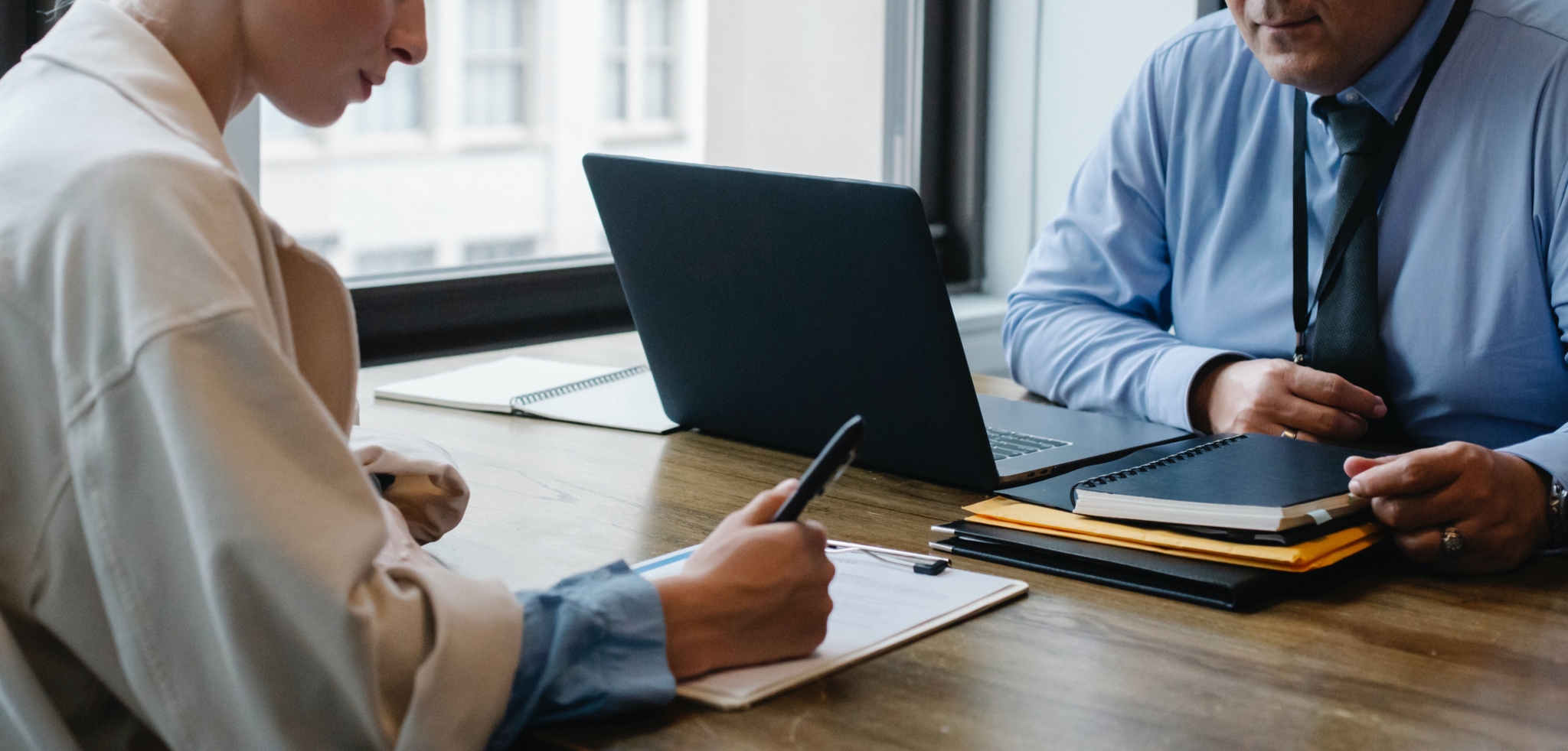 Two people in an office setting, one on a laptop the other writing on a paper.